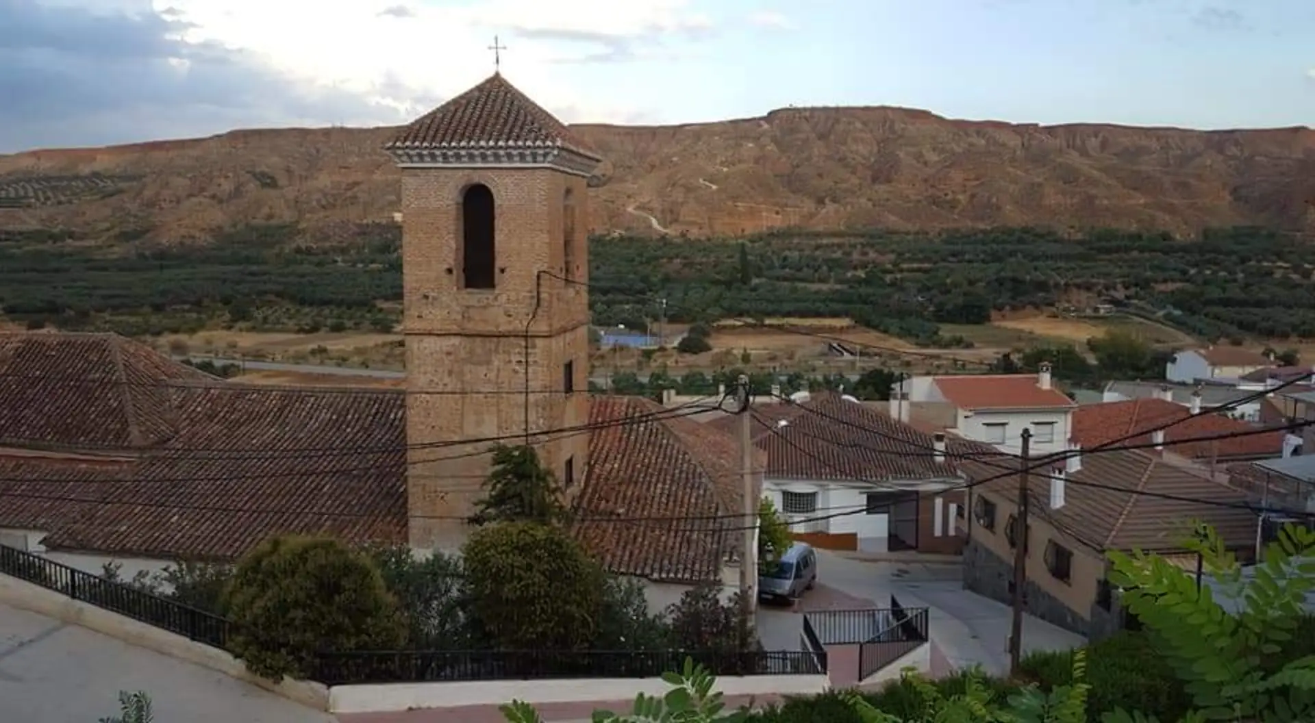 Campanario de la iglesia elevándose sobre los tejados árabes con el fondo rojizo de las cárcavas