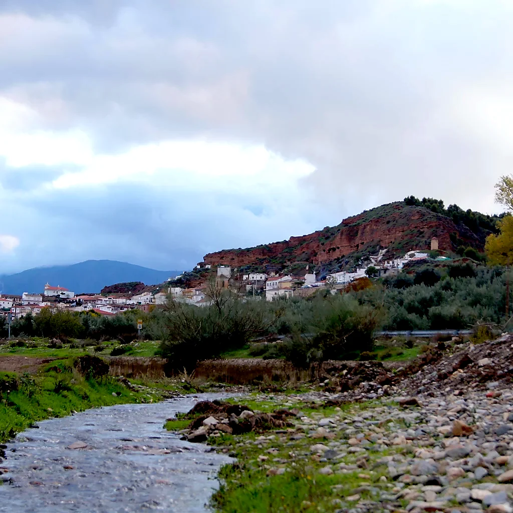 Río Alhama en primer plano con Beas de Guadix al fondo bajo un cielo de tormenta